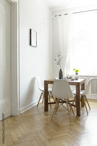 Wooden dining table with flowers in vase, two mugs and four chairs in real photo of bright room interior with window with drapes © Photographee.eu