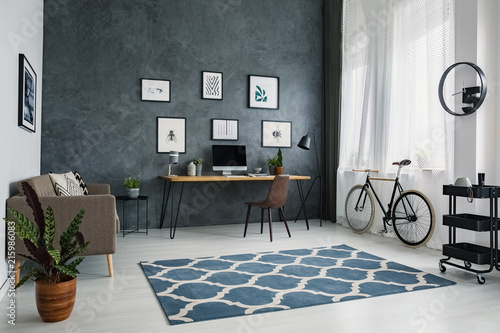 Patterned carpet in bright workspace interior with bicycle next to brown chair at desk. Real photo photo