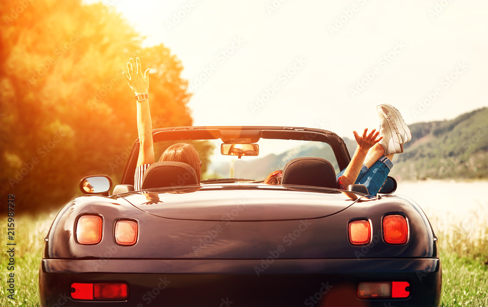 Two girls travelers sit in cabriolet car and enjoy with beautiful view - obrazy, fototapety, plakaty 