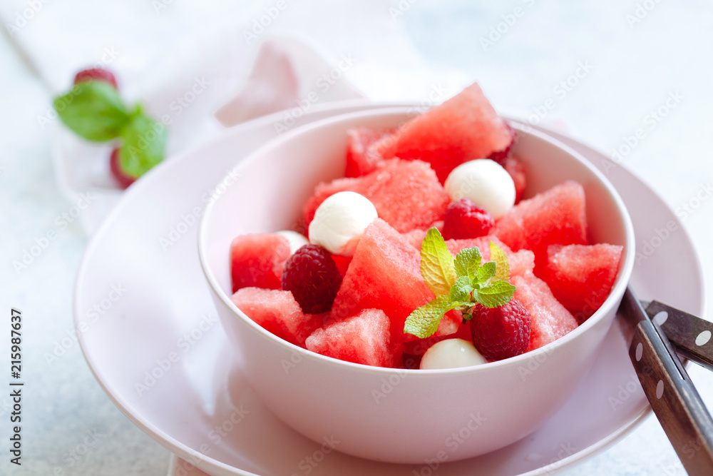 Watermelon salad with raspberry and mozzarella in pink bowl on white table Watermelon salad with raspberry and mozzarella in pink bowl on white table
