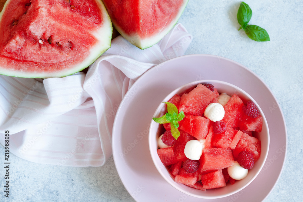 Watermelon salad with raspberry and mozzarella in pink bowl on white table Watermelon salad with raspberry and mozzarella in pink bowl on white table