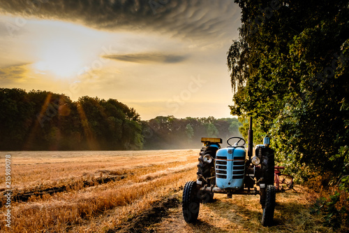 Old tractor in a field on a summer morning with the sun coming up