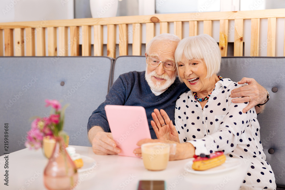 Hello daughter. Optimistic senior couple applying tablet and woman waving hand Hello daughter. Optimistic senior couple applying tablet and woman waving hand