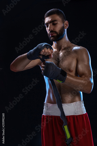 Boxer preparing her gloves for a fight. Photo of muscular man strapping up hands on black background. photo