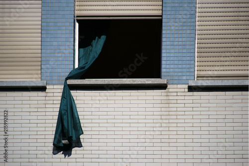 Gardine weht aus dem Fenster / Eine lose Gardine weht aus dem Fenster eines verklinkerten Wohngebäudes.
