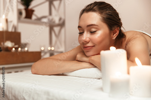 Beautiful woman lies in massage room in spa over candles.