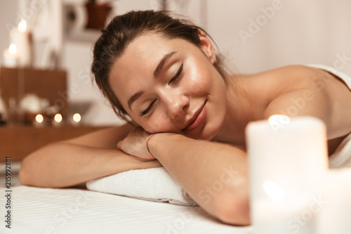 Beautiful woman lies in massage room in spa over candles.