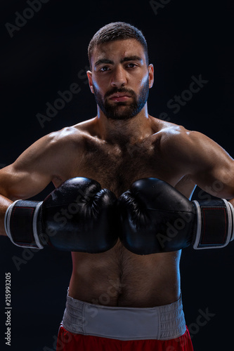 Portrait of tough male boxer posing in boxing stance against black background. © nazarovsergey