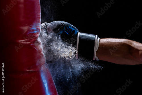 Close-up hand of boxer at the moment of impact on punching bag over black background © nazarovsergey