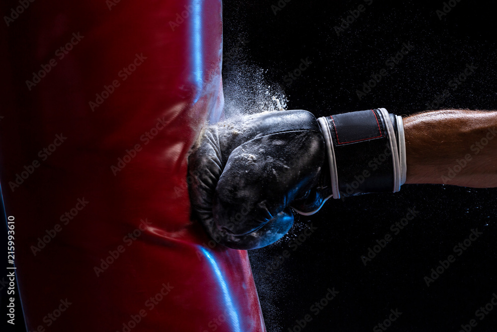 Close-up hand of boxer at the moment of impact on punching bag over black background - obrazy, fototapety, plakaty 