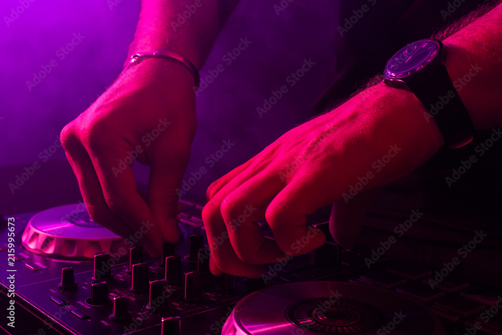 Fototapeta Dj mixing on turntables with color light effects. Soft focus on hand. Close-up.