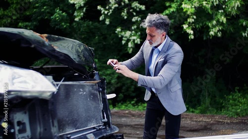 Mature man taking pictures of a broken car after an accident.