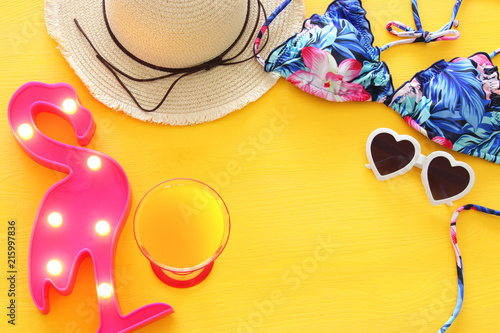 Top view of fashion female swimsuit bikini and white fedora hat over yellow wooden background. Summer beach vacation concept.