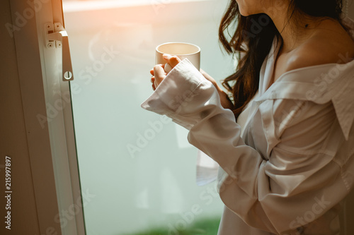 Woman holding a glass of coffee in the window in the morning.