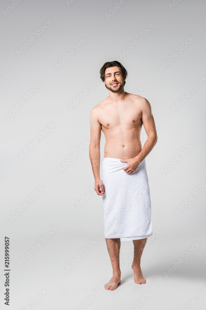 smiling handsome man in white towel on grey backdrop