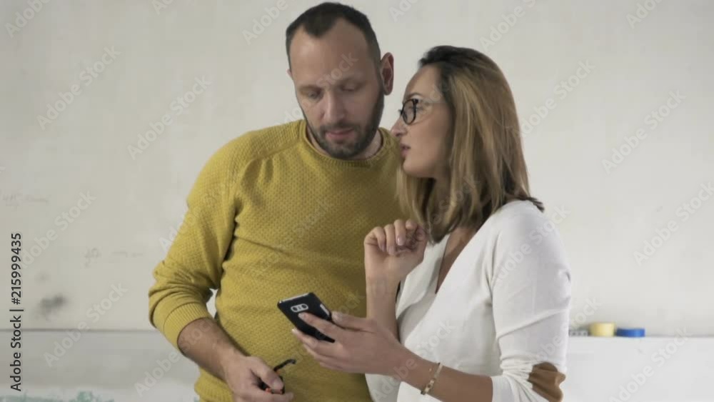Young couple talking and checking project on smartphone at new home
Young couple talking and checking project on smartphone at new home