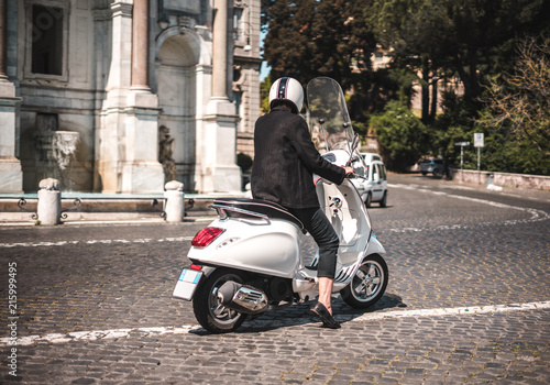 Modern and fashionable woman on a scooter   vespa in Roma Italy on a beautiful day with historic background  fontana del Gianicolo 