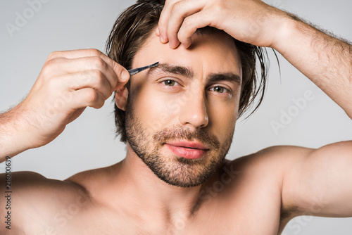 portrait of young man with tweezers looking at camera isolated on grey