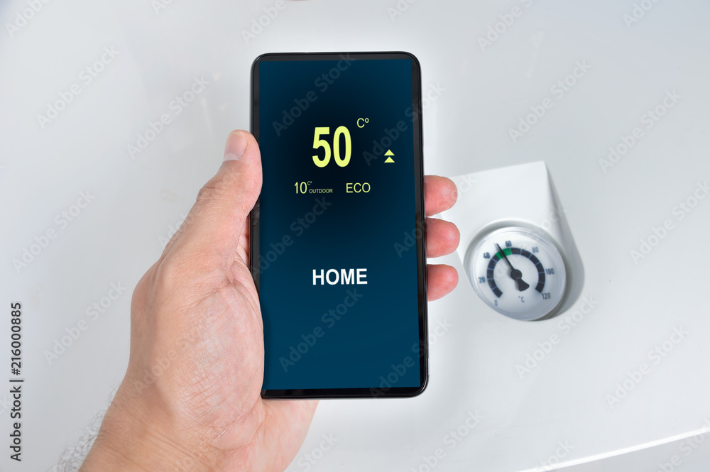 close up of a person hand adjusting temperature on thermostat through smart phone at home close up of a person hand adjusting temperature on thermostat through smart phone at home