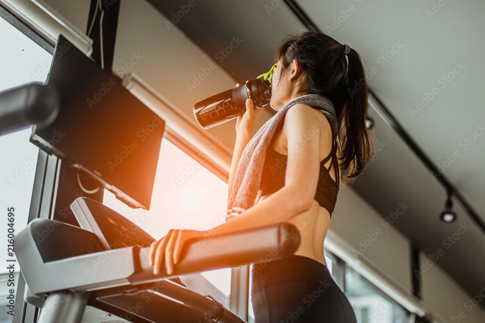 © Garun Studios - Young woman at treadmill drinking water.Young woman at treadmill drinking .protein shake.