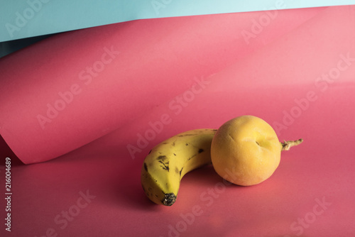 Bodegón minimalista de melocotón y plátano sobre un fondo de colores rosa y azul