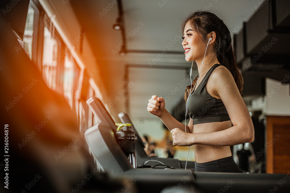 Portrait of Fitness woman running on treadmill in gym listening to music.exercising concept.fitness and healthy lifestyle.