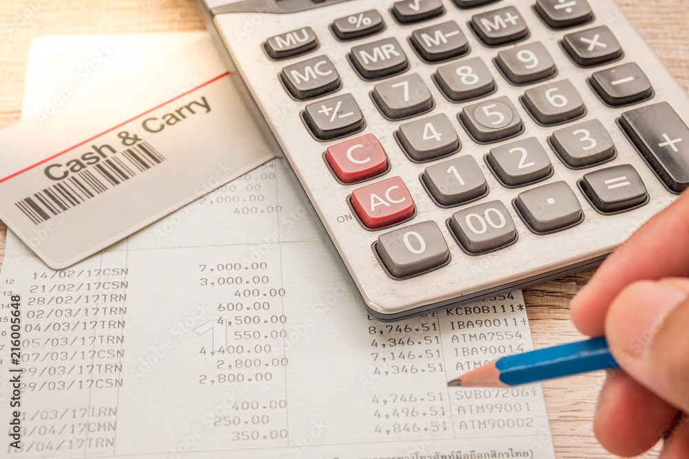 The fingers are holding the pencil. Below is a calculator, a bank book, a cash card placed on a wooden desk. The fingers are holding the pencil. Below is a calculator, a bank book, a cash card placed on a wooden desk.