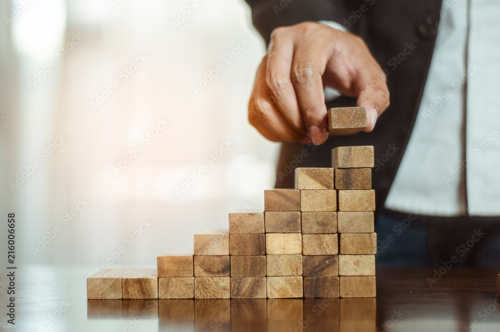 plan and strategy in business.risk concept.hand of man has piling up and stacking a wooden block.Businessman Building The Success. plan and strategy in business.risk concept.hand of man has piling up and stacking a wooden block.Businessman Building The Success.