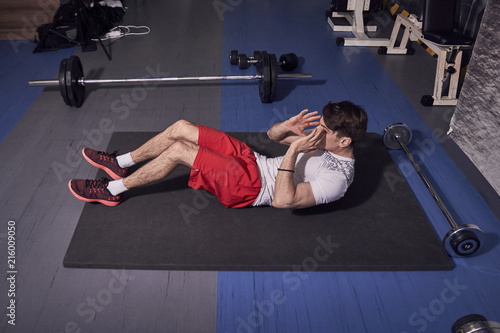 one young man, abs exercise, laying on floor mat, gym indoors, elevated view.