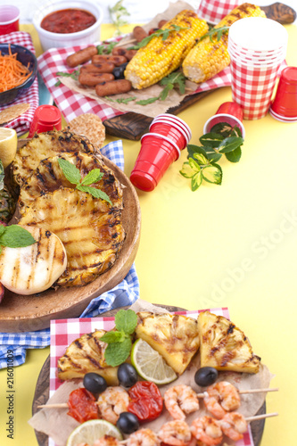 Fototapeta Naklejka Na Ścianę i Meble -  Picnic with grilled food. Sausages and corn on barbecue, shrimp, vegetables and fruits. Delicious summer lunch and plastic dishes. Top view