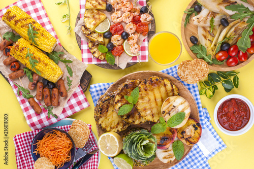 Picnic with grilled food. Sausages and corn on barbecue, shrimp, vegetables and fruits. Delicious summer lunch and plastic dishes. Top view