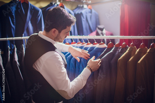 Tailor, tailoring. Men's suit, tailor in his workshop. Elegant man's suits hanging in row. Luxury mens classic suits on rack in elegant men's boutique. photo