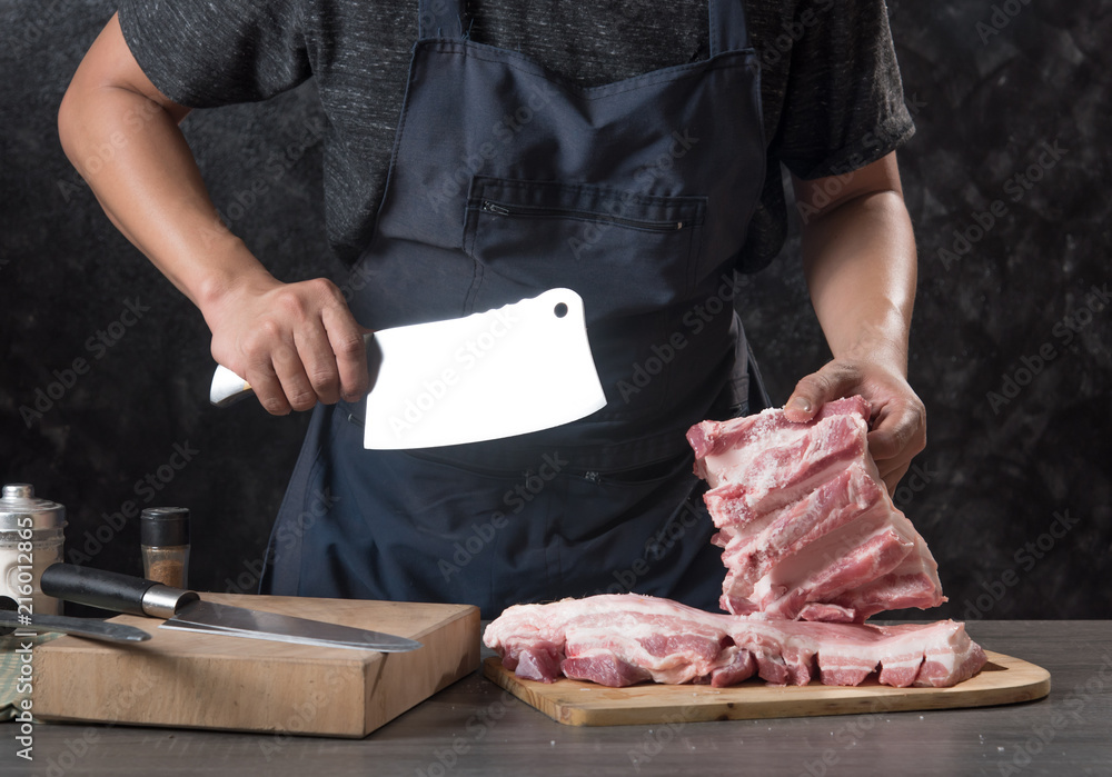 Chef cook cuts large piece of pork meat on wooden cutting board with knife,concept of cooking