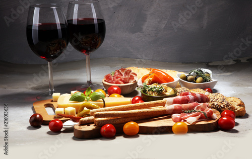 Italian antipasti wine snacks set. Cheese variety, Mediterranean olives, crudo, Prosciutto di Parma, salami and wine in glasses over stone grunge background.