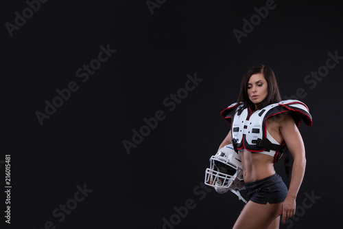 Portrait of sexy attractive young girl in a sports outfit for rugby with the helmet strongly looking forward standing on black background