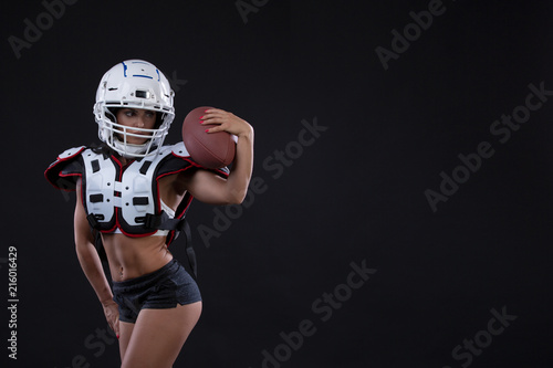 Portrait of sexy attractive young girl in a sports outfit for rugby with the helmet strongly looking forward standing on black background