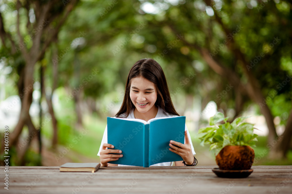 Obraz premium Asian girl reading book at park in summer sunset light. asian woman reading book in Thailand. asian Beautiful woman reading a book at table.