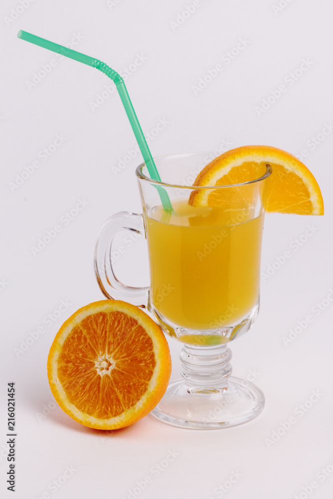 Orange juice in a transparent glass with a green straw, next to it lies half an orange on a white background. Concept of food and drinks. Orange juice in a transparent glass with a green straw, next to it lies half an orange on a white background. Concept of food and drinks.