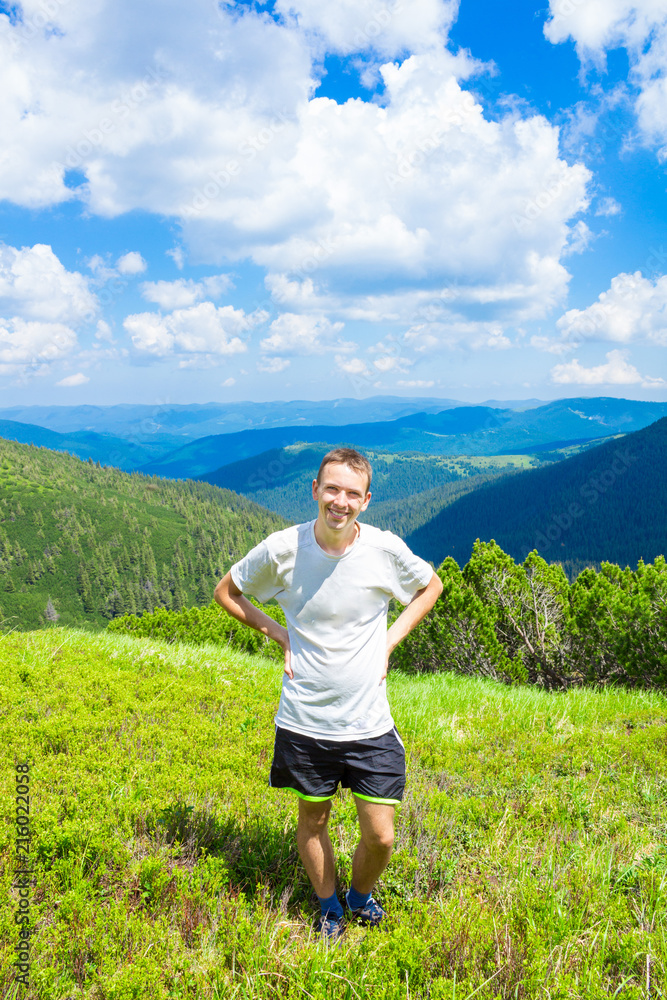 Happy man on top of mountain admiring beautiful valley view in summer day
