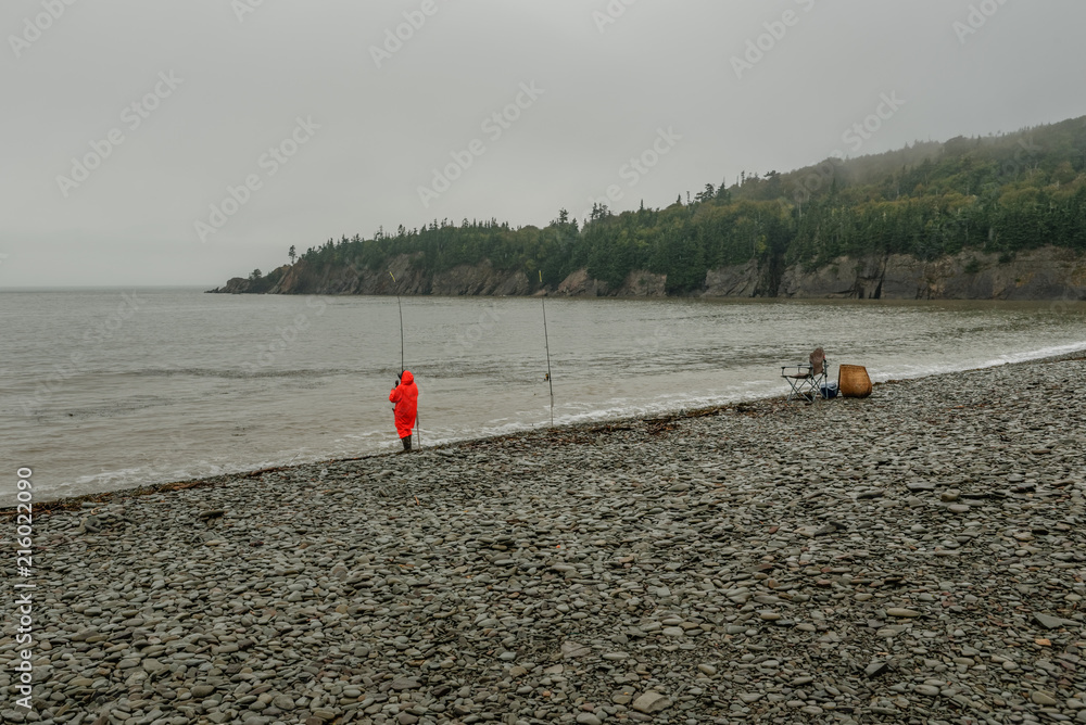 Φωτογραφία lone fisherman in bright orange rain gear on a rainy day at the foggy coast with