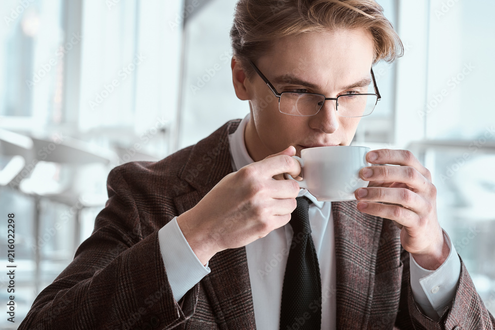 Young businessman in eyeglasses at office sitting drinking coffe