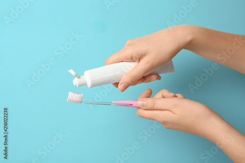 Woman squeezing toothpaste on brush against color background