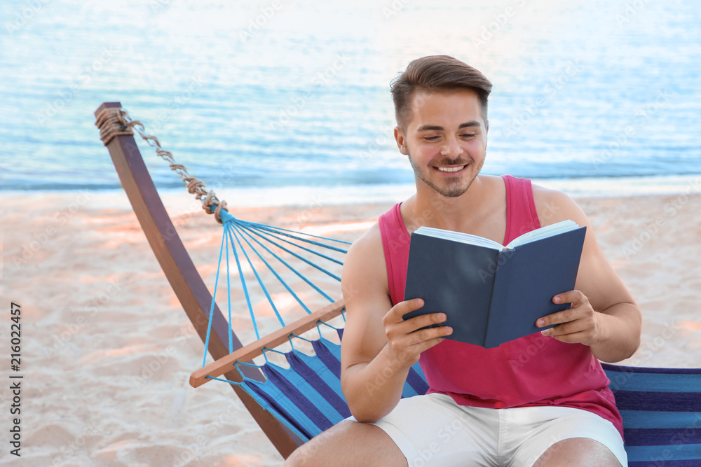 Obraz premium Young man reading book in hammock at seaside