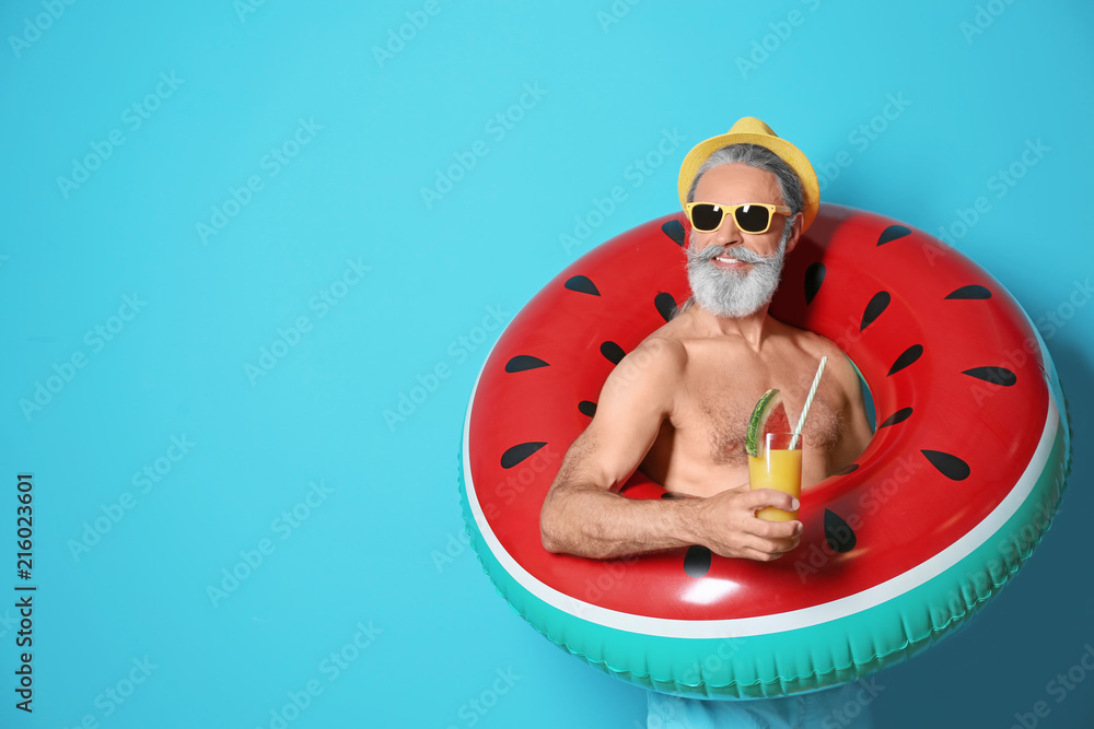 Obraz premium Shirtless man with inflatable ring and glass of cocktail on color background