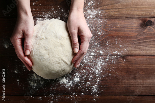 Female hands holding raw dough on wooden table