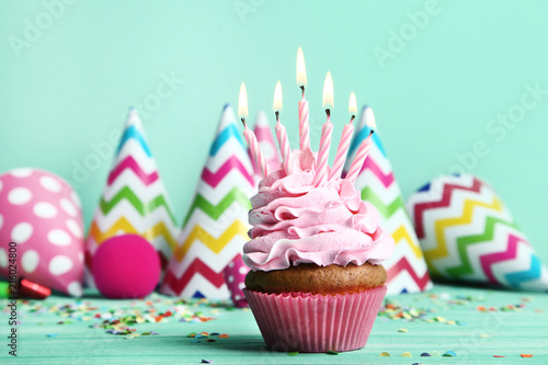 Cupcake with candles and paper caps on green background