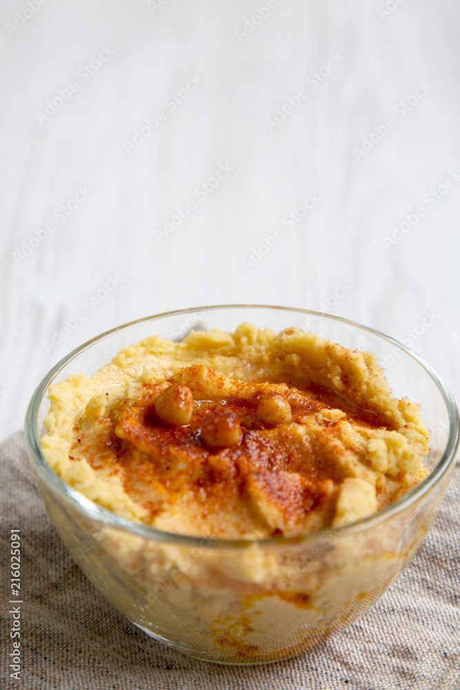 Bowl of Hummus with roasted chickpeas, paprika, olive oil on a white wooden table, side view. Closeup.