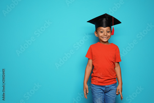 Little African-American school child with graduate cap on color background photo