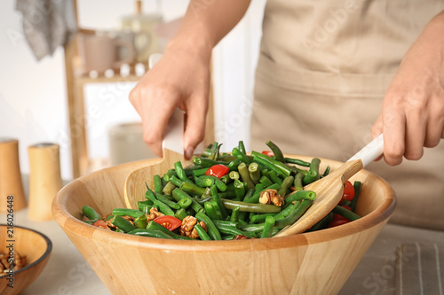 Woman preparing healthy salad with green beans, cherry tomatoes and walnuts at table
