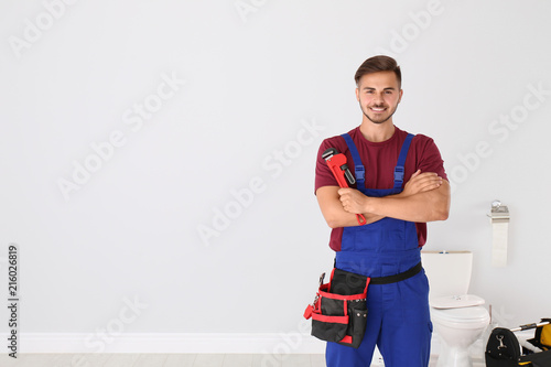 Young man with plumber wrench and toilet bowl on background photo